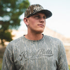Guy wearing Washed Mossy Oak long sleeve shirt and Mossy Oak Bottomland hat with Ridge Belts Hunting Co. logos