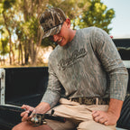 Guy fishing in Mossy Oak washed long sleeve and Bottomland rope hat on truck tailgate