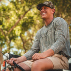 Guy wearing Washed Mossy Oak long sleeve shirt and Mossy Oak Bottomland in the trees.
