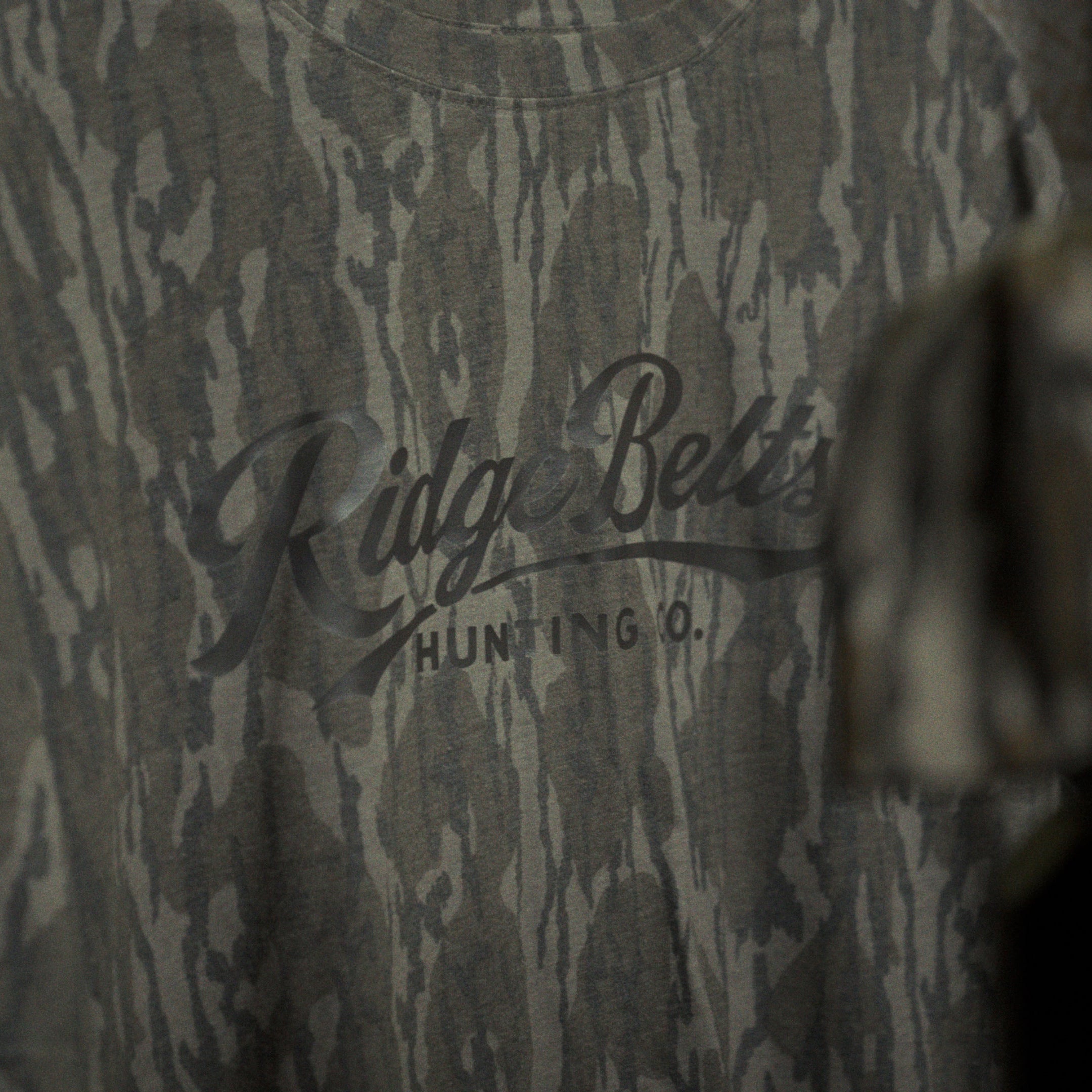 Camo-patterned shirt with 'Ridge Belts' branding and a cap in the foreground.